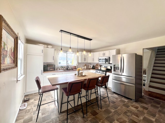 kitchen with a sink, decorative backsplash, white cabinets, appliances with stainless steel finishes, and pendant lighting