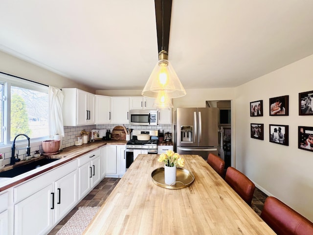 kitchen featuring backsplash, butcher block counters, appliances with stainless steel finishes, white cabinets, and a sink