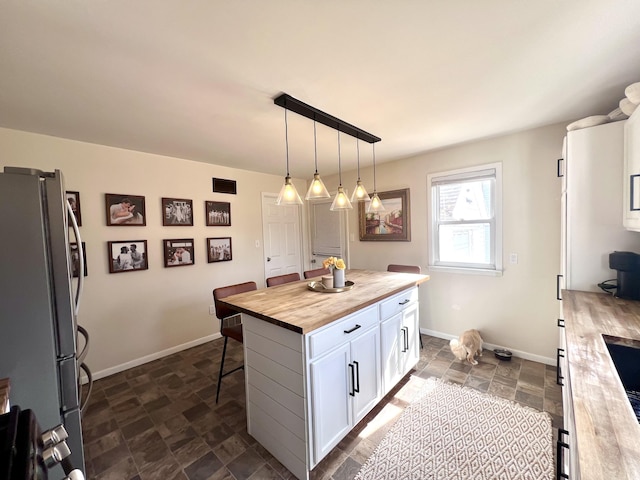 kitchen with stone finish flooring, butcher block counters, a breakfast bar area, freestanding refrigerator, and white cabinetry