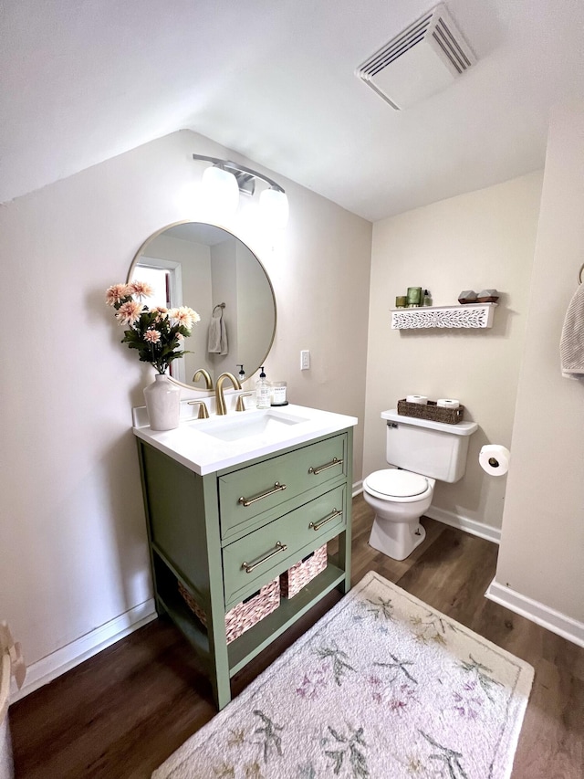 half bath with vanity, wood finished floors, visible vents, baseboards, and toilet