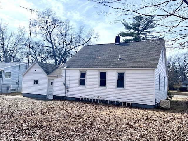 back of house with a chimney and roof with shingles