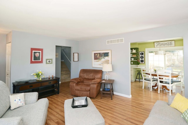 living room featuring stairway, wood finished floors, visible vents, and baseboards