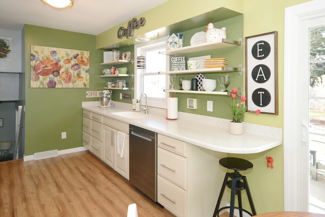 kitchen featuring light wood-type flooring, a sink, open shelves, stainless steel dishwasher, and light countertops