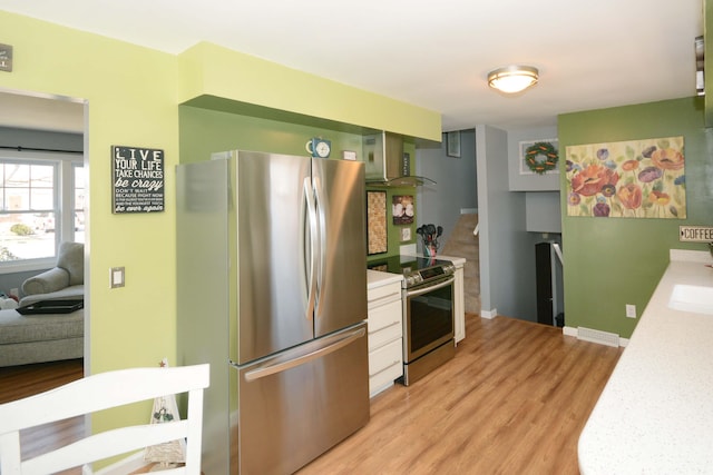 kitchen with a sink, stainless steel appliances, wall chimney exhaust hood, light wood finished floors, and light countertops