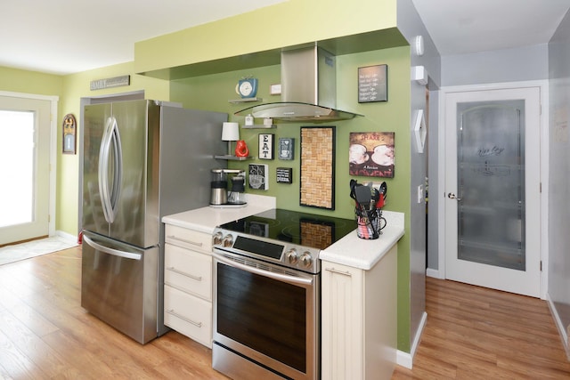 kitchen with light wood-style floors, appliances with stainless steel finishes, wall chimney exhaust hood, and light countertops