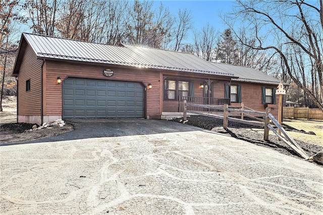 chalet / cabin featuring aphalt driveway, a porch, metal roof, and an attached garage