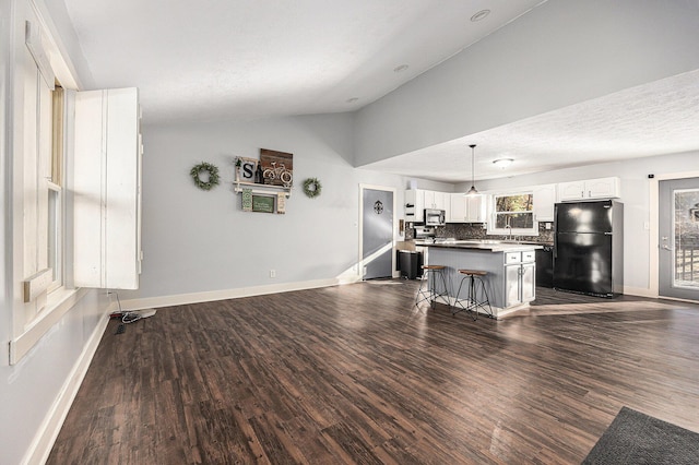 kitchen with stainless steel microwave, a center island, freestanding refrigerator, white cabinets, and vaulted ceiling