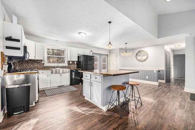 kitchen with black appliances, a sink, a kitchen breakfast bar, dark wood-style floors, and white cabinets