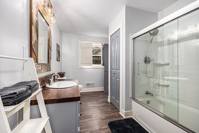 bathroom featuring vanity, wood finished floors, visible vents, bath / shower combo with glass door, and toilet