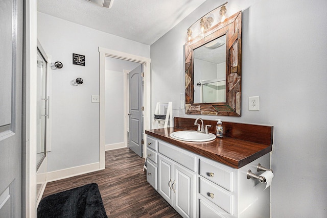 bathroom featuring vanity, wood finished floors, baseboards, a stall shower, and a textured ceiling