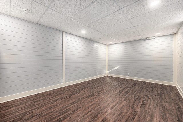 unfurnished room with dark wood-style floors, a drop ceiling, and baseboards