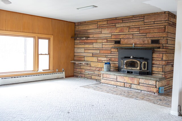 unfurnished living room with baseboard heating, a wood stove, wooden walls, and carpet floors