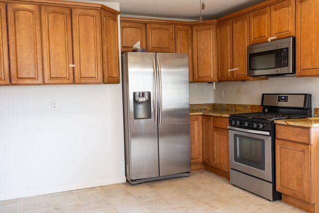 kitchen with brown cabinets, stone countertops, stainless steel appliances, and baseboards