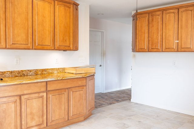 kitchen featuring light stone counters, brown cabinetry, and baseboards