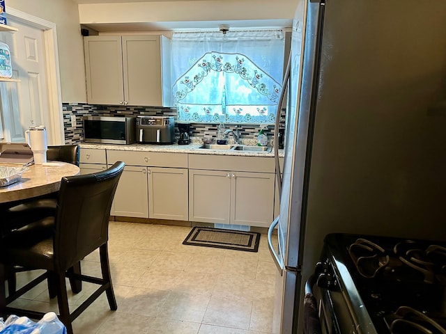 kitchen featuring light tile patterned floors, a sink, decorative backsplash, light countertops, and stainless steel appliances