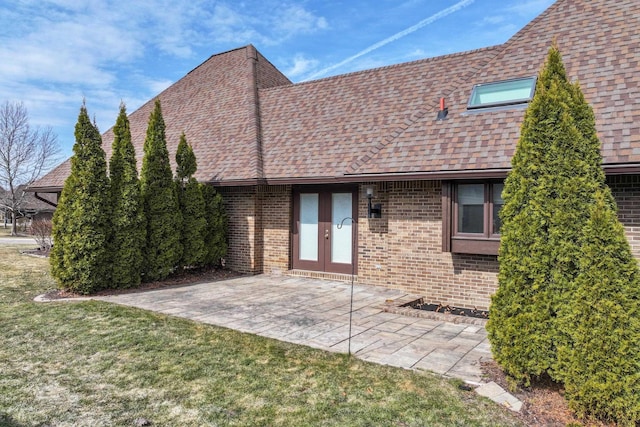 rear view of property featuring brick siding, a shingled roof, a lawn, french doors, and a patio area