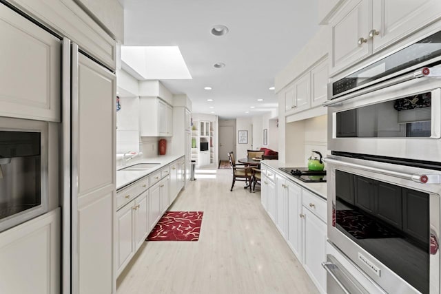 kitchen featuring stainless steel double oven, light wood-style flooring, light countertops, white cabinetry, and black electric cooktop