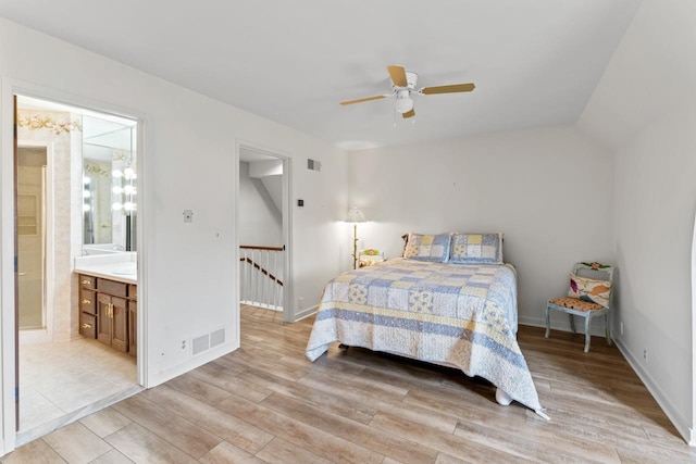 bedroom featuring visible vents, light wood-style flooring, ensuite bathroom, and lofted ceiling