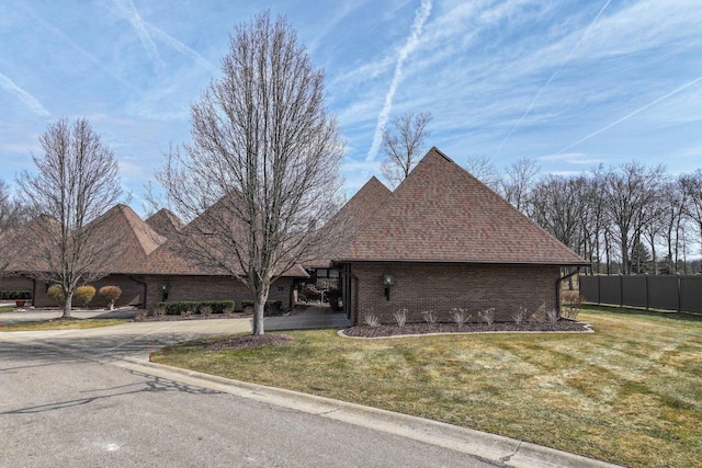 view of front of home featuring brick siding, a shingled roof, a front lawn, and fence