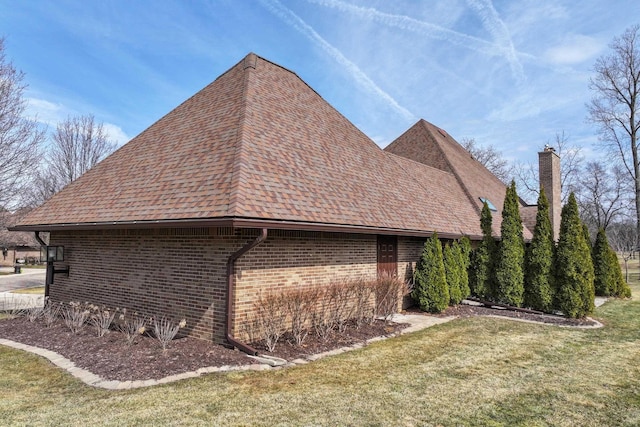 view of side of home with brick siding, a chimney, a lawn, and roof with shingles