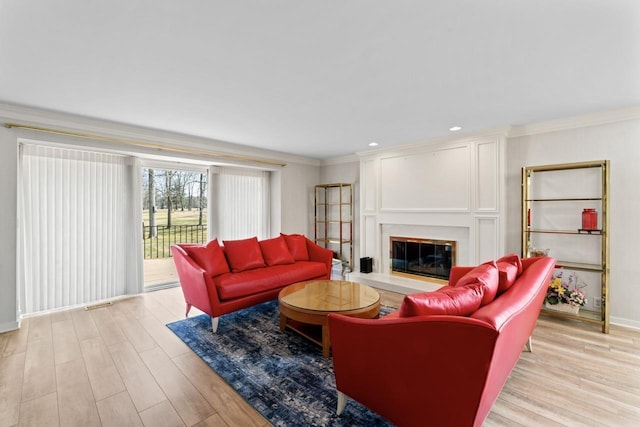 living room with baseboards, ornamental molding, recessed lighting, light wood-style floors, and a glass covered fireplace