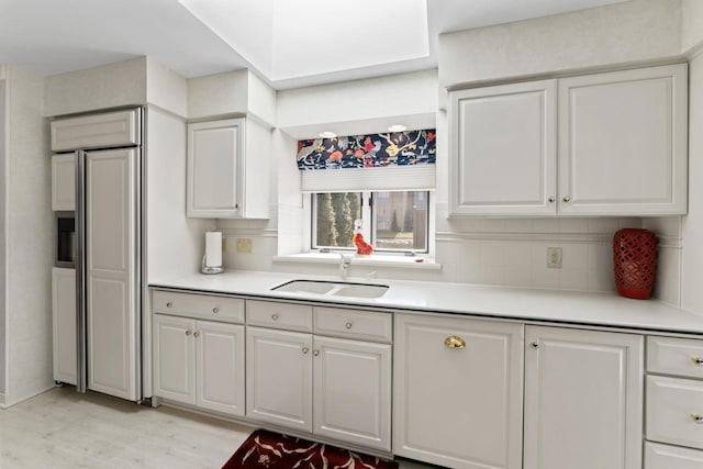 kitchen with tasteful backsplash, white cabinetry, light countertops, and a sink