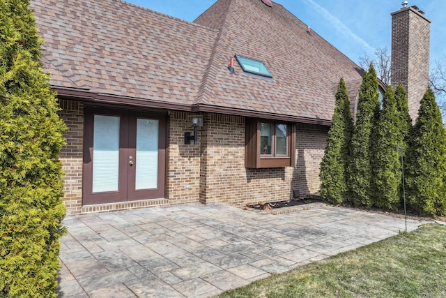 back of house with french doors, a shingled roof, brick siding, a chimney, and a patio area