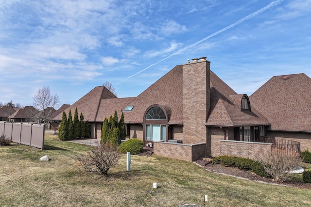 view of front of property with a front yard, fence, roof with shingles, a chimney, and brick siding