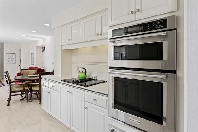 kitchen featuring white cabinets, light wood-style flooring, tasteful backsplash, and stainless steel double oven