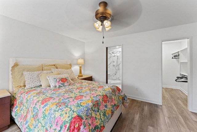 bedroom featuring a walk in closet, light wood-style flooring, ensuite bath, baseboards, and ceiling fan