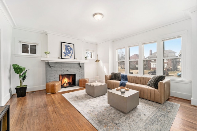 living room featuring ornamental molding, a brick fireplace, baseboards, and hardwood / wood-style floors