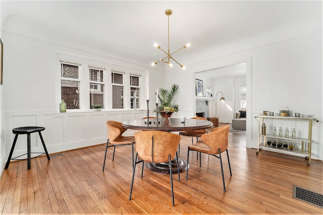 dining room featuring light wood finished floors, visible vents, a brick fireplace, a notable chandelier, and a decorative wall