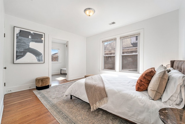 bedroom featuring visible vents, multiple windows, wood finished floors, and baseboards