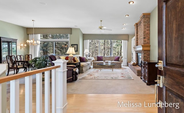 living room with light wood-style flooring, a brick fireplace, and ceiling fan with notable chandelier