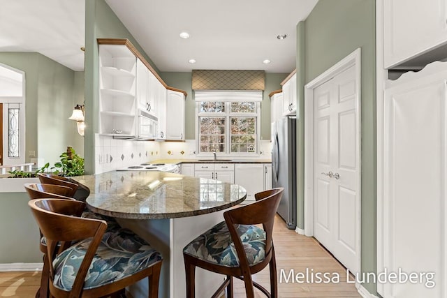 kitchen featuring white microwave, white cabinetry, a peninsula, open shelves, and a kitchen bar