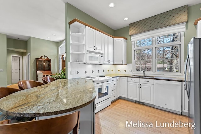 kitchen with open shelves, dark stone countertops, a sink, white appliances, and a peninsula