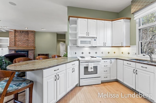 kitchen with a breakfast bar area, a fireplace, a peninsula, white appliances, and a sink