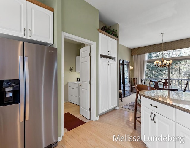 kitchen with light stone counters, white cabinets, stainless steel fridge with ice dispenser, washer / dryer, and a chandelier