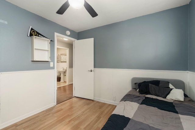 bedroom featuring light wood-style flooring, a ceiling fan, and wainscoting