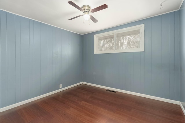 empty room with ceiling fan, visible vents, baseboards, and dark wood finished floors