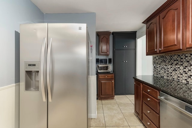 kitchen with backsplash, dark stone counters, appliances with stainless steel finishes, light tile patterned flooring, and wainscoting