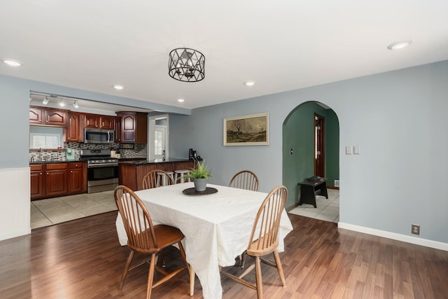 dining room featuring arched walkways, recessed lighting, baseboards, and light wood-style floors