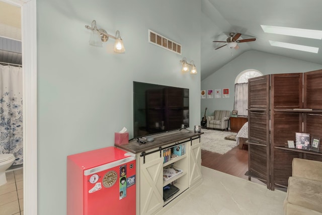 living room with tile patterned flooring, visible vents, vaulted ceiling with skylight, and ceiling fan