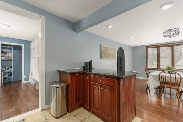 bar featuring baseboards, arched walkways, light wood-style floors, and beam ceiling