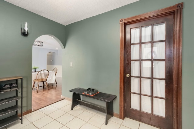 hallway featuring light tile patterned floors, baseboards, arched walkways, and a textured ceiling