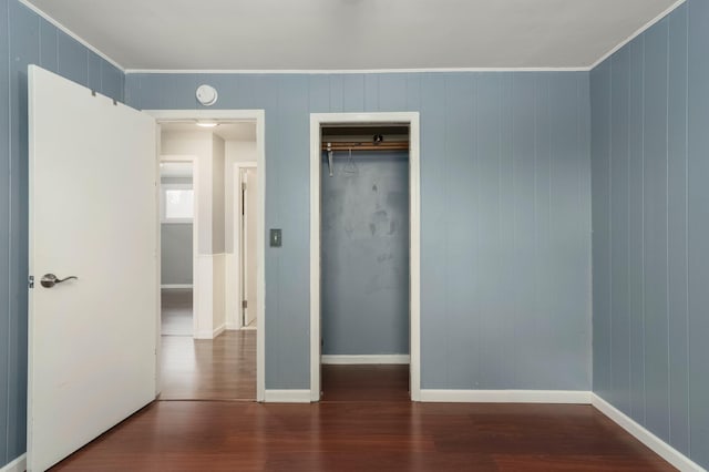 unfurnished bedroom with a closet, crown molding, baseboards, and wood finished floors