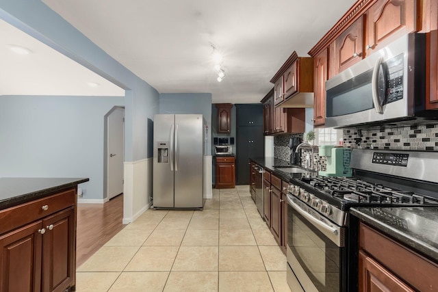 kitchen with light tile patterned floors, decorative backsplash, rail lighting, stainless steel appliances, and a sink