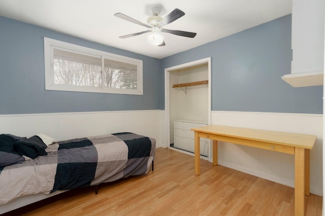 bedroom with a closet, wainscoting, ceiling fan, and wood finished floors