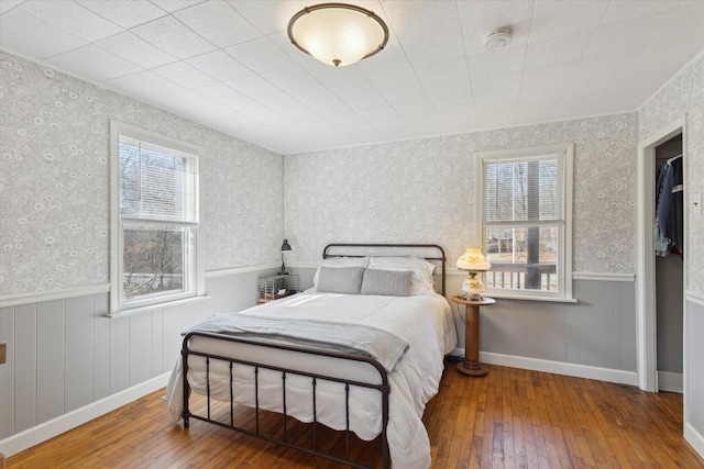 bedroom with wallpapered walls, multiple windows, and a wainscoted wall