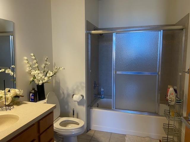 full bath featuring vanity, tile patterned floors, toilet, and combined bath / shower with glass door